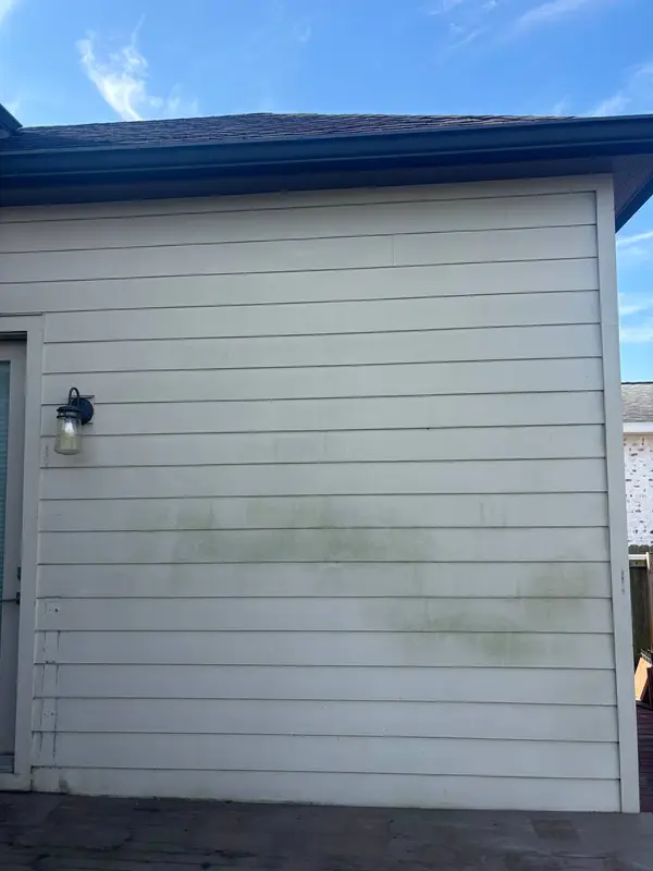 Light grey lap siding carrying green algae staining, with a black wall lantern on the left and a dark deck edge across the bottom.