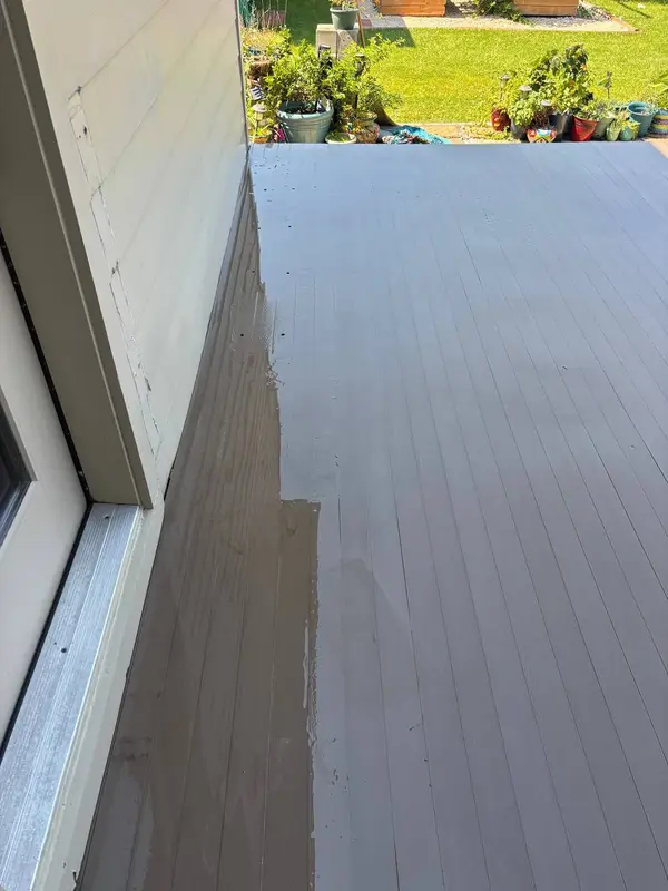 A run of wooden deck boards, wet and dark on the left and dry on the right, beside the house siding.