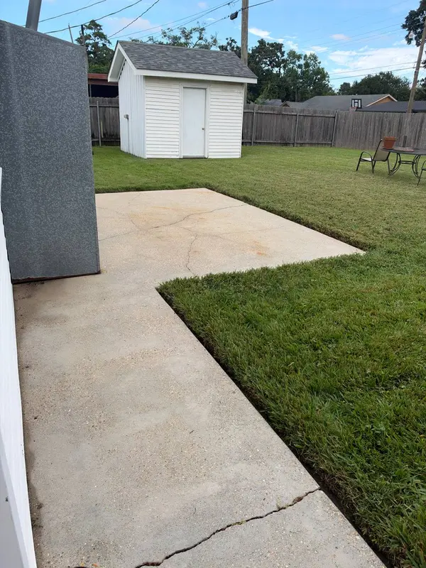 A cracked concrete patio with orange staining, a white shed and a table and chairs on the grass beyond.