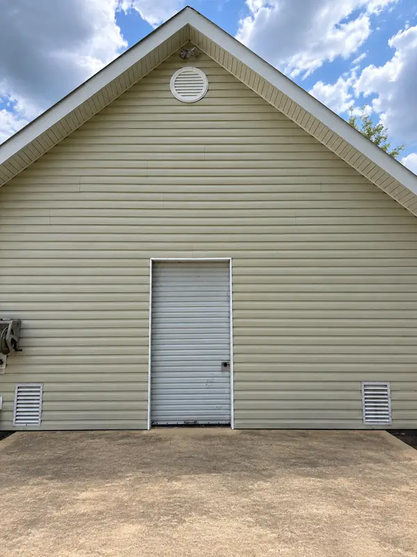 The gable end of a beige sided garage with a roll up door, two louvred vents and two floodlights above a stained concrete pad.