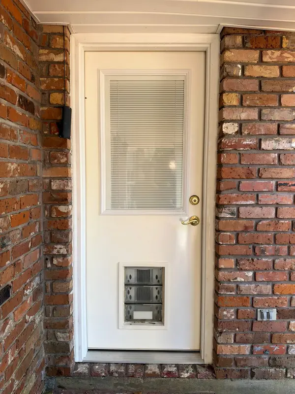 A white exterior door with a windowed upper half and a pet door set into a red brick wall.