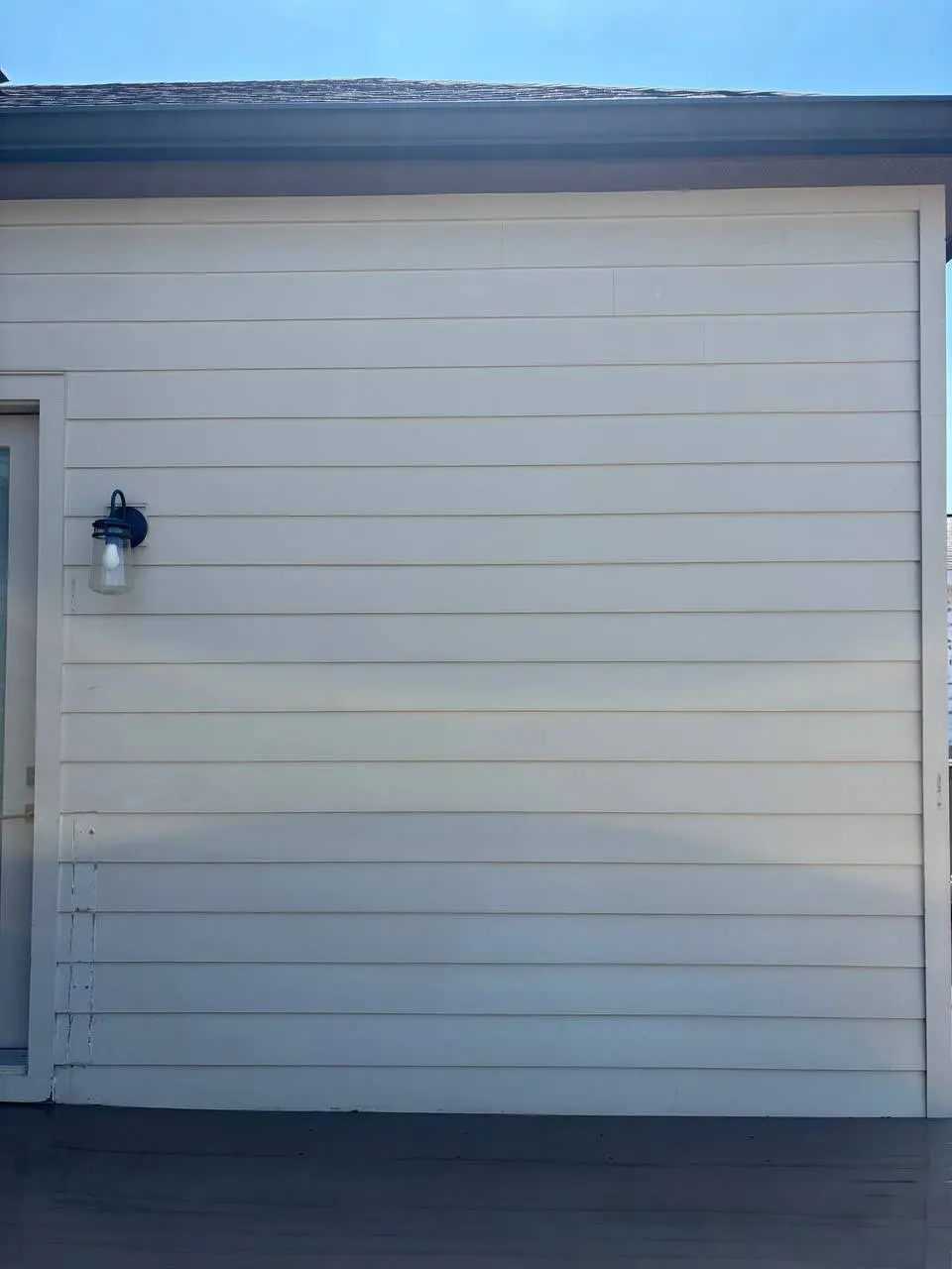 A lap sided wall with a black lantern lamp on the left and a dark porch floor below.