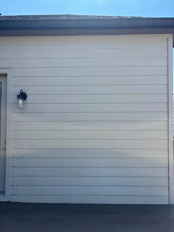 A lap sided wall with a black lantern lamp on the left and a dark porch floor below.