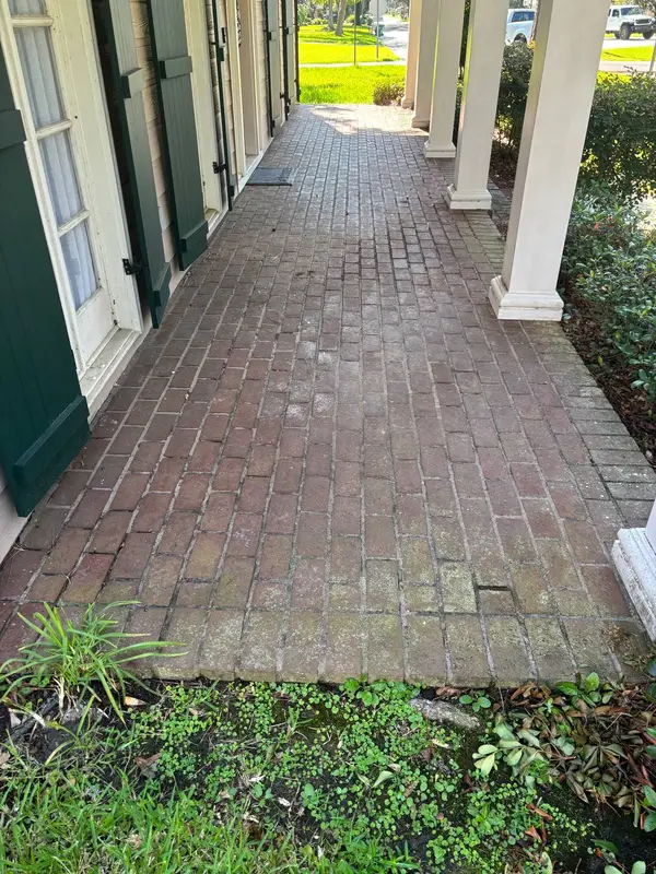 A red brick porch floor with a wet sheen, beside beige siding with dark green shutters and white columns.