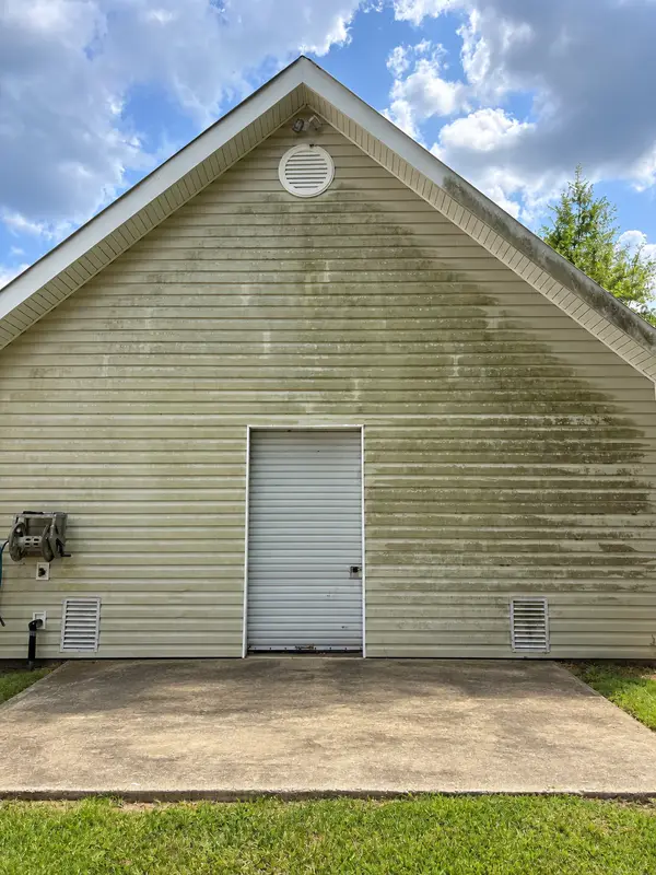 A brick porch floor with moss patches between white columns, beside beige siding and green shutters.