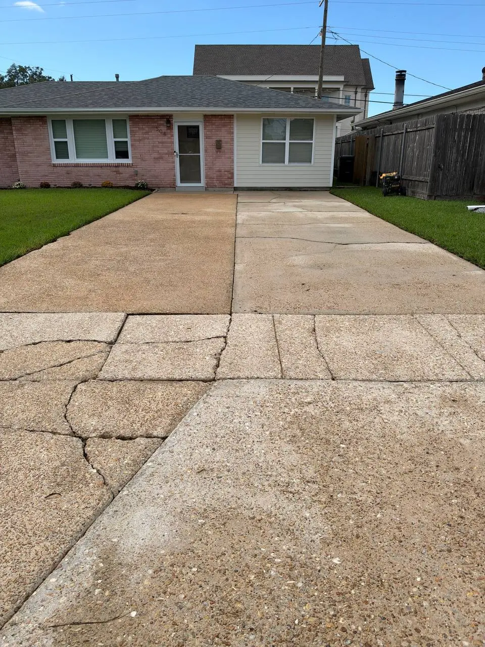 A single storey home in brick and siding above a cracked, stained concrete driveway and lawn.