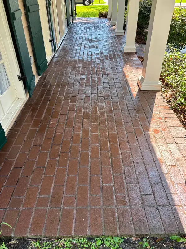 A red brick porch floor that looks freshly washed and wet, beside beige siding with green shutters and white square columns.