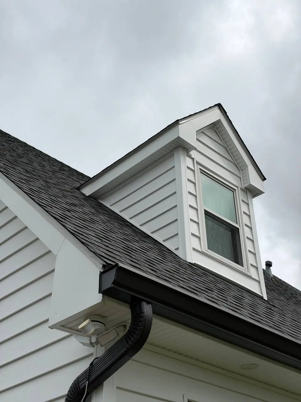 A dormer window above a black half round gutter line, with a security light under the eave.