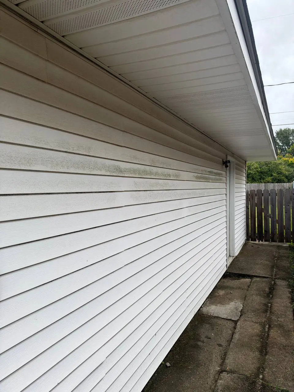 A white siding wall with dark mildew streaks running along the middle panels beside a concrete walkway.