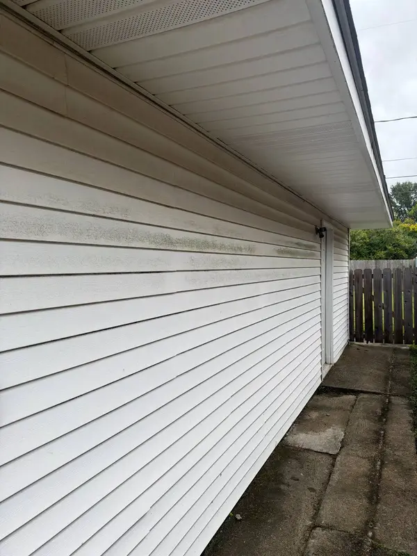 A white siding wall with dark mildew streaks running along the middle panels beside a concrete walkway.