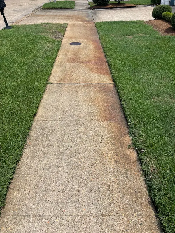 A concrete sidewalk heavily stained with rust coloured streaks around an embedded utility cover.