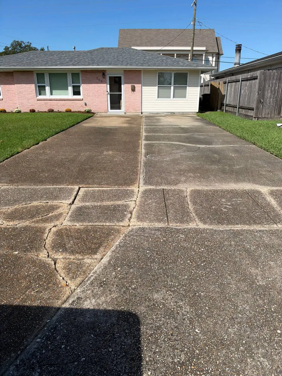 A house in pink brick and beige siding above a cracked, stained concrete driveway, with the house number 506 on the wall.