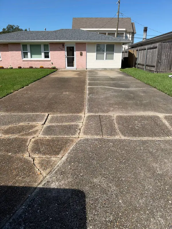 A house in pink brick and beige siding above a cracked, stained concrete driveway, with the house number 506 on the wall.