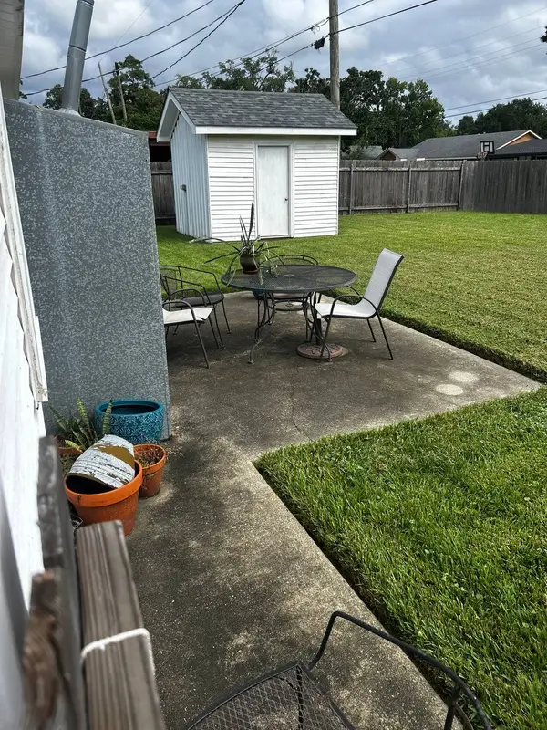 A patio with a concrete slab, a round black wire table with four chairs, and potted plants along a metal wall.