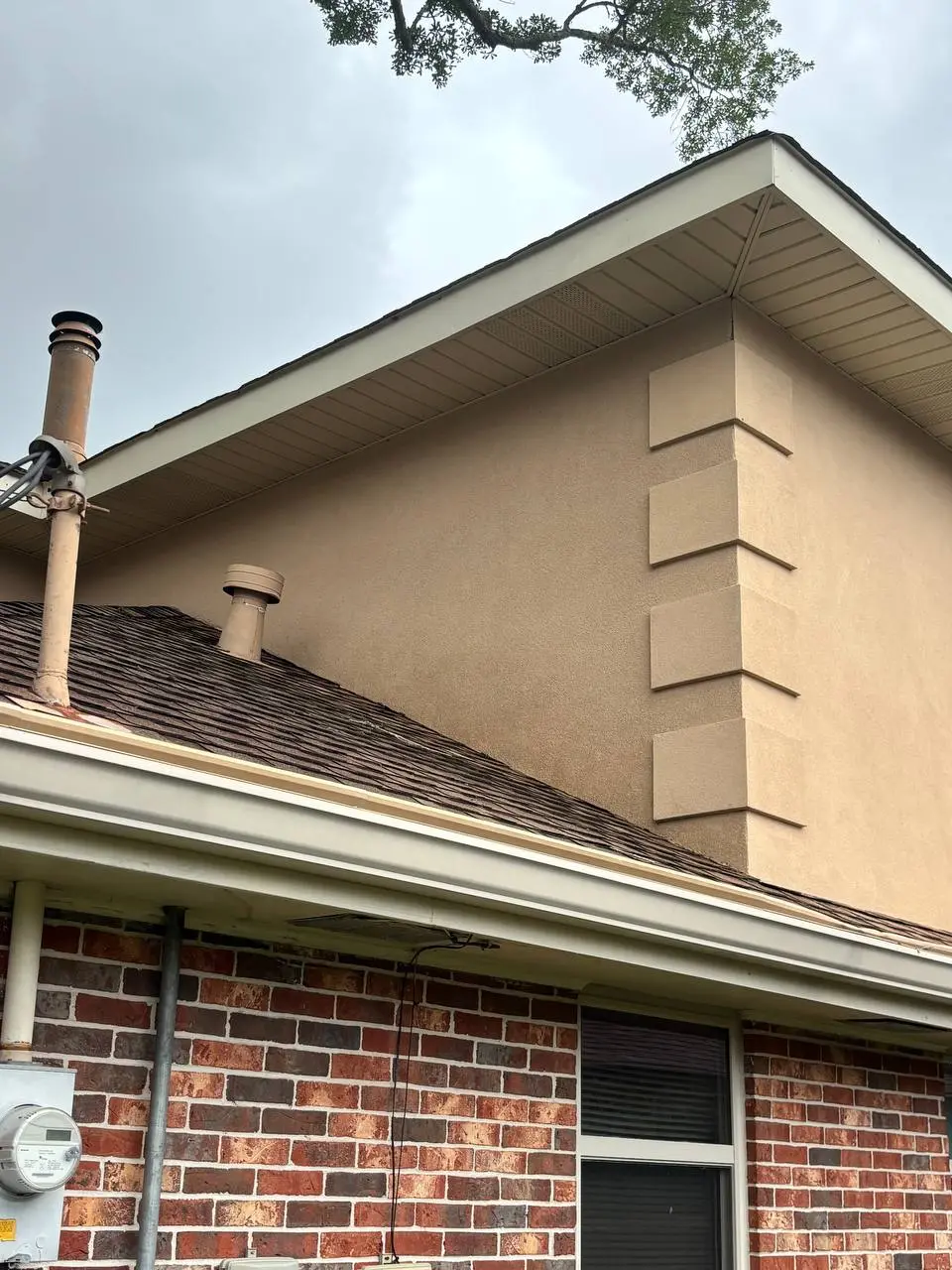 After cleaning: the tan stucco wall with its stacked panels and brick base, with the heavy staining gone.