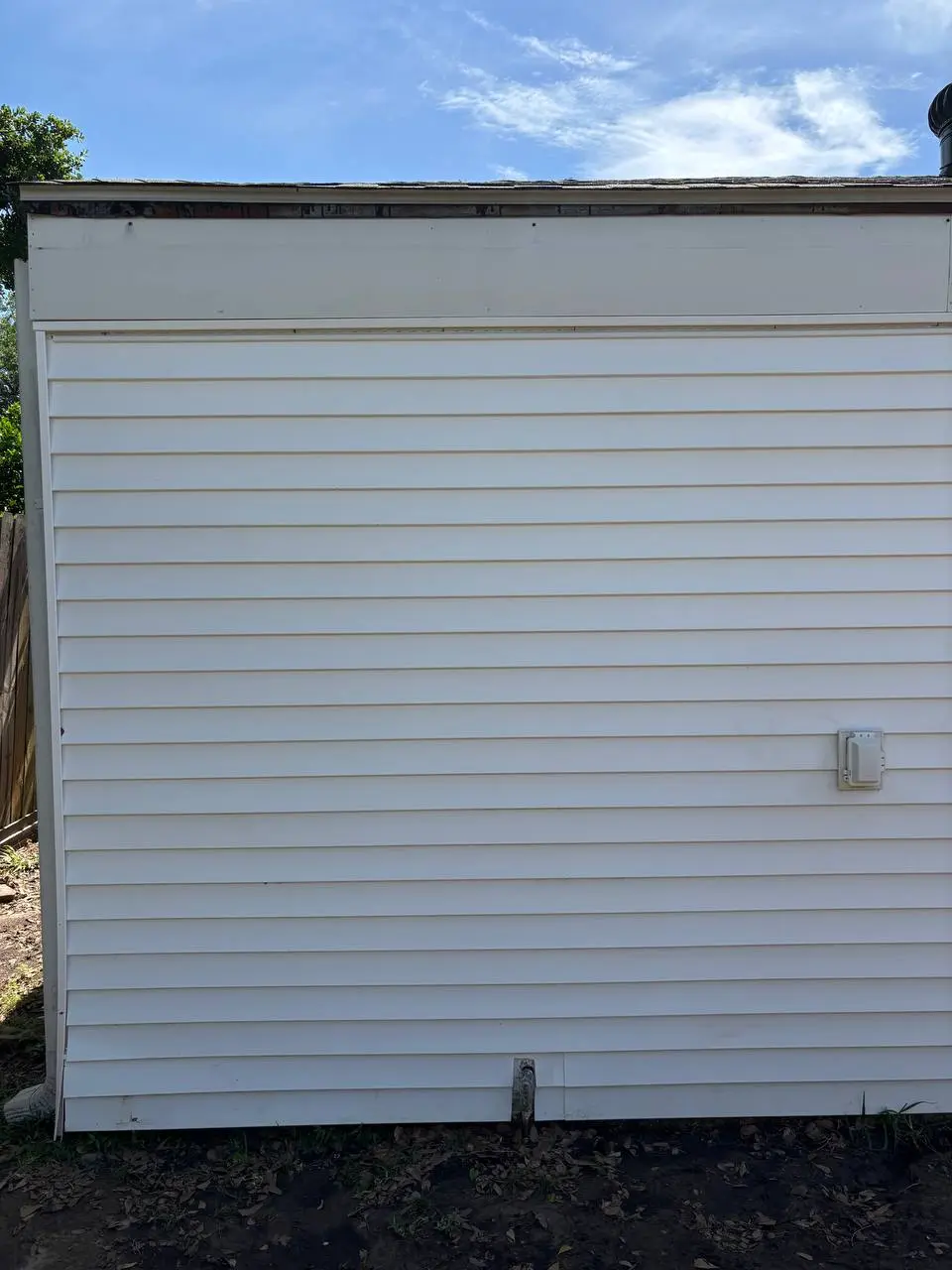 After cleaning: a white sided wall with an electrical junction box, with green staining still along the left of the frame.